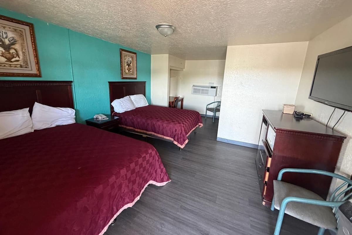 A hotel room with two beds, a desk, a chair, a television, and a framed picture on the wall.