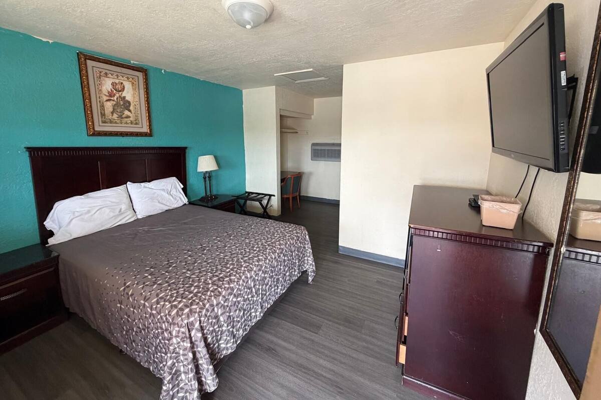 A hotel room with a bed, a desk, a television, and a picture on the wall.