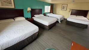 Una habitación de hotel con cuatro camas, una ventana con cortinas, un reloj de pared y una lámpara en el techo.