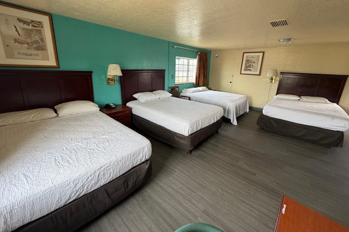 A hotel room with four beds, a window with curtains, a wall clock, and a ceiling light fixture.