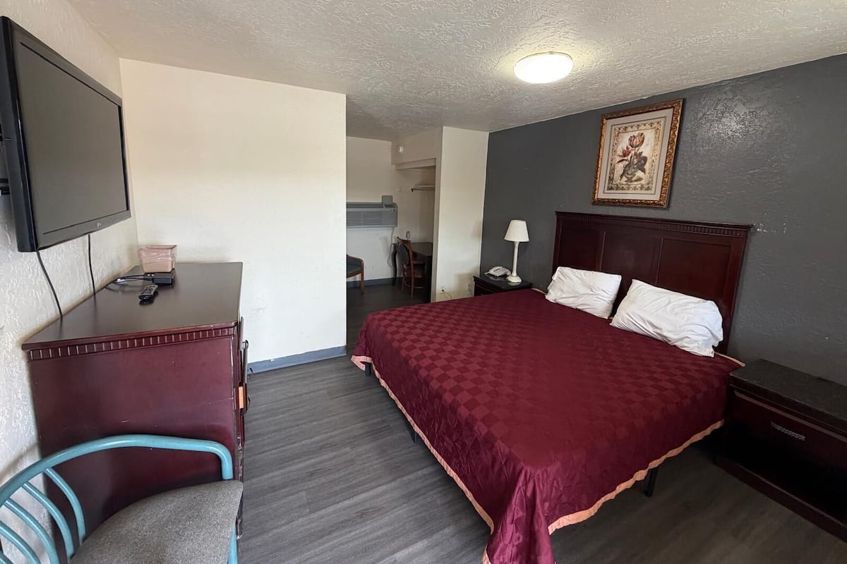 A hotel room with a bed, a desk, a chair, a television, and a painting on the wall.