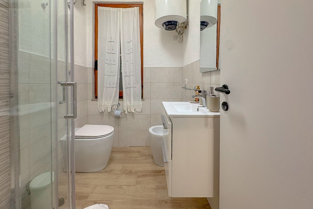 Un bagno con cabina doccia in vetro, un water, un bidet, un lavandino con specchio e un portasciugamani.