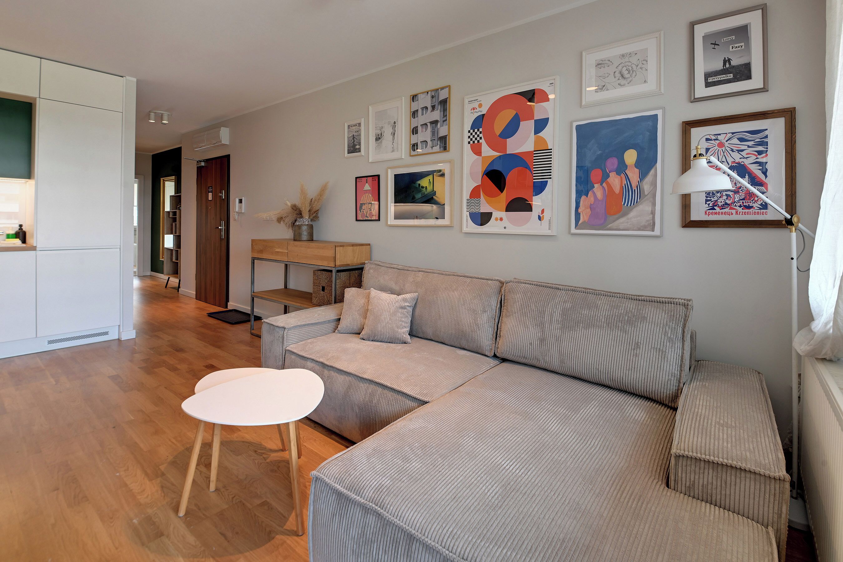 Un salon moderne avec un canapé, une petite table et une lampe. Des tableaux encadrés ornent le mur.