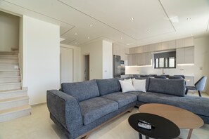 Ein modernes Wohnzimmer mit einer grauen Eckcouch, einem Holztisch und einer Treppe, die zu einer anderen Ebene führt.