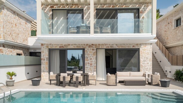 Ein modernes, zweistöckiges Haus mit Pool, Sitzgelegenheit im Freien und einer Fassade aus Naturstein.