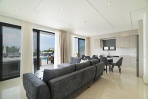 Ein modernes Wohnzimmer mit einer grauen Eckcouch, einem Esstisch mit Stühlen und einer Küchenzeile mit weißen Schränken sowie einem Flachbildfernseher.
