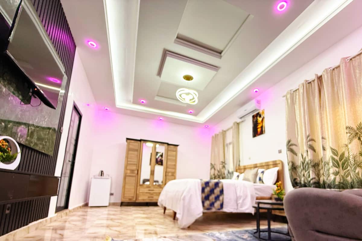 Un dormitorio moderno con cama, una silla, un espejo e iluminación empotrada en el techo.