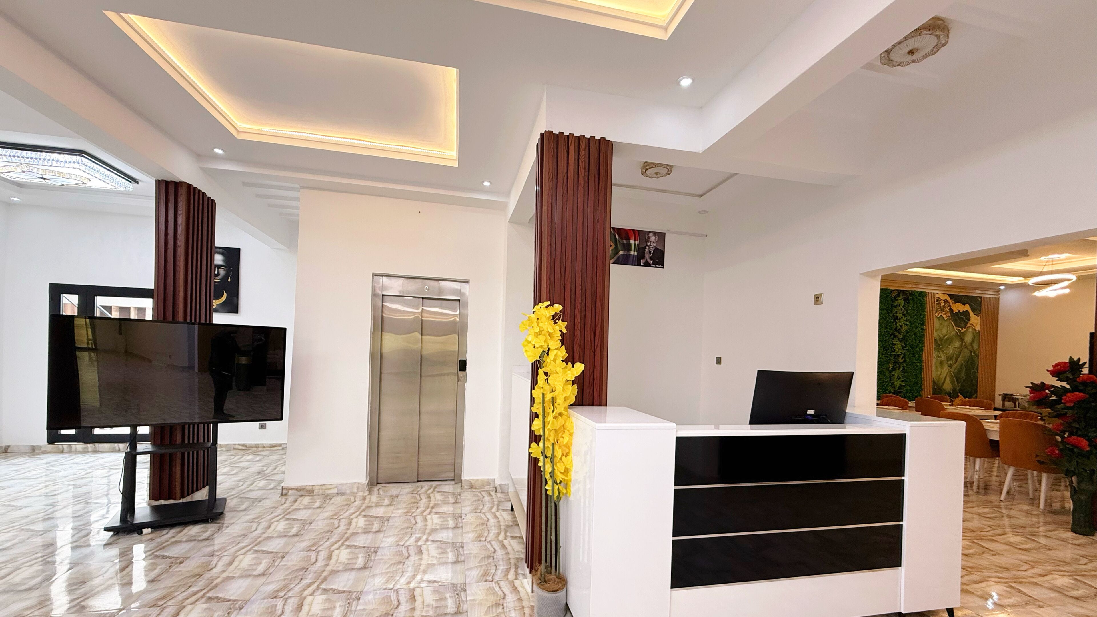 A hotel lobby with a reception desk, a television, an elevator, and a dining area.