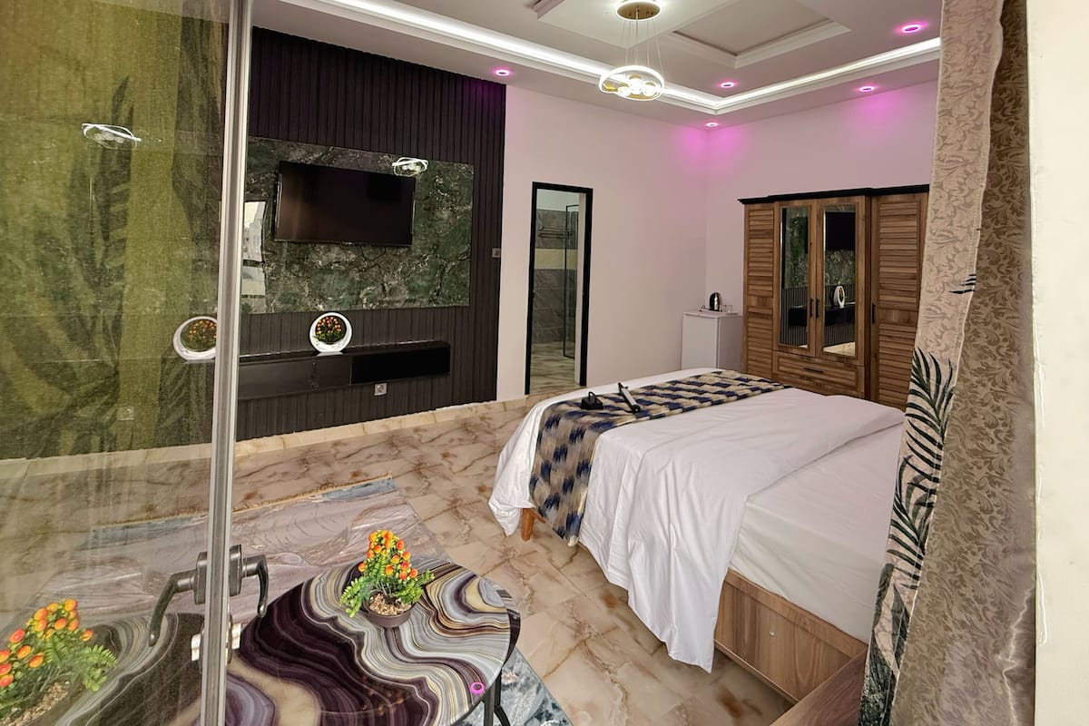 Un dormitorio con una cama grande, televisión, espejo, armario y suelo de mármol.