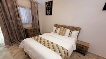 Un dormitorio con cama, mesitas de noche, cabecera de madera, una obra de arte en la pared y una ventana con cortinas.