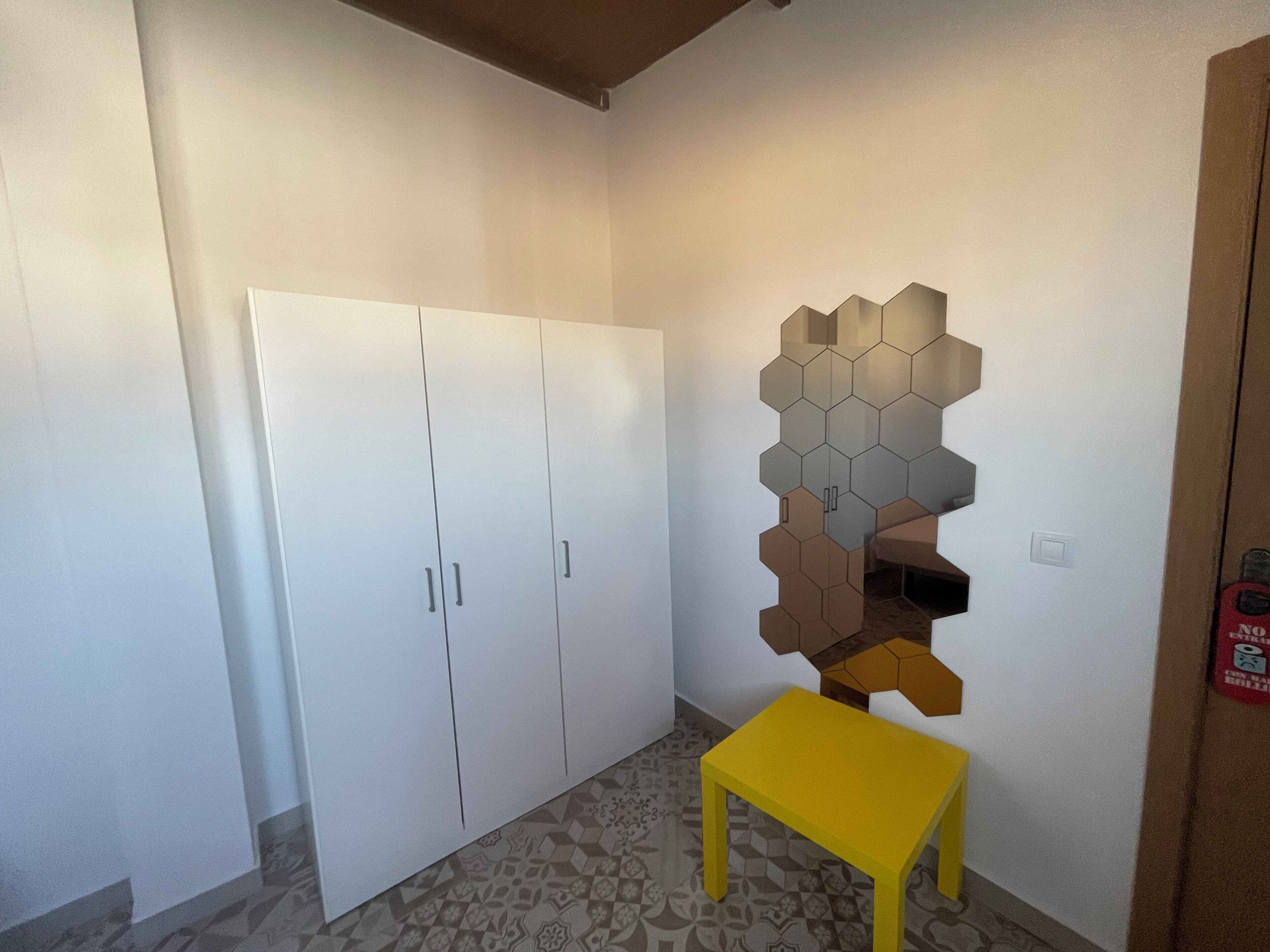 A room with a white wardrobe, a yellow bench, and a wall with a geometric pattern.