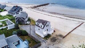Een woongebied aan de kust met huizen direct naast een strand, met een mix van eenlaags en meerlaags gebouwen, zichtbare opritten en voortuinen.
