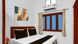 Ein Hotelzimmer mit Bett, einem Kunstwerk an der Wand, einer Klimaanlage und einem Fenster mit Vorhängen.