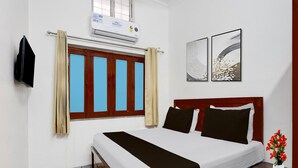 Ein Hotelzimmer mit Bett, einem Vorhangfenster, einer Klimaanlage und zwei gerahmten Bildern an der Wand.