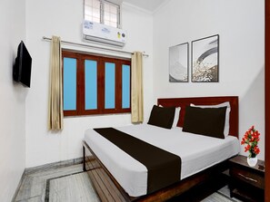 Ein Hotelzimmer mit Bett, einem Vorhangfenster, einer Klimaanlage und zwei gerahmten Bildern an der Wand.
