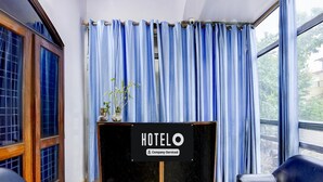 Ein Hotelrezeptionsschalter mit einem Schild, zwei schwarzen Ledersessel und ein Fenster mit blauen Vorhängen.
