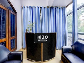 Ein Hotelrezeptionsschalter mit einem Schild, zwei schwarzen Ledersessel und ein Fenster mit blauen Vorhängen.