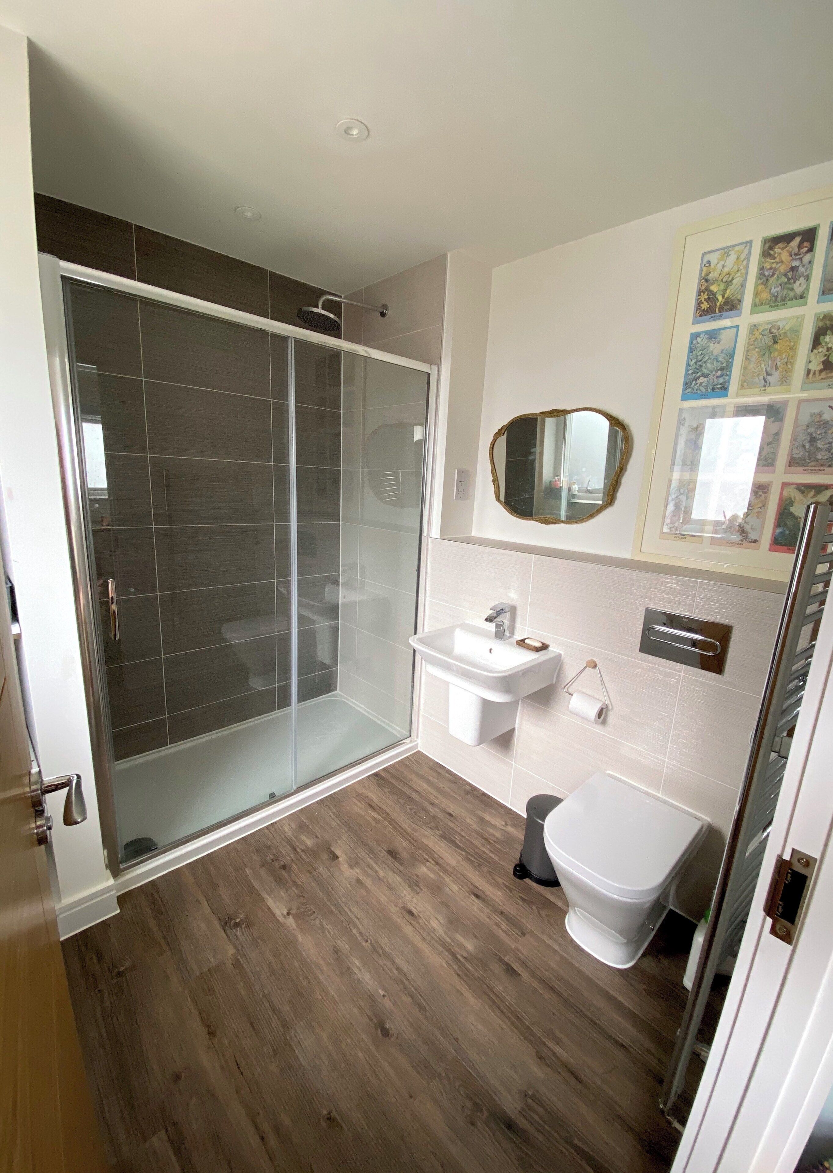 Une salle de bain avec une douche à parois de verre, un lavabo blanc, des toilettes et un miroir doté d’un cadre décoratif.