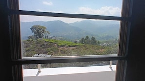 Una ventana con vistas a un paisaje montañoso, que incluye un árbol destacado y edificios a lo lejos.
