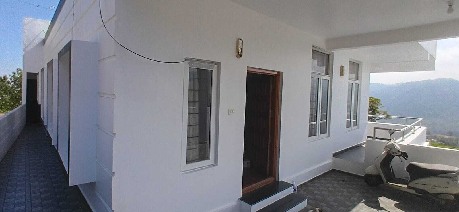 A white building with a covered outdoor area, a scooter, and a view of mountains.