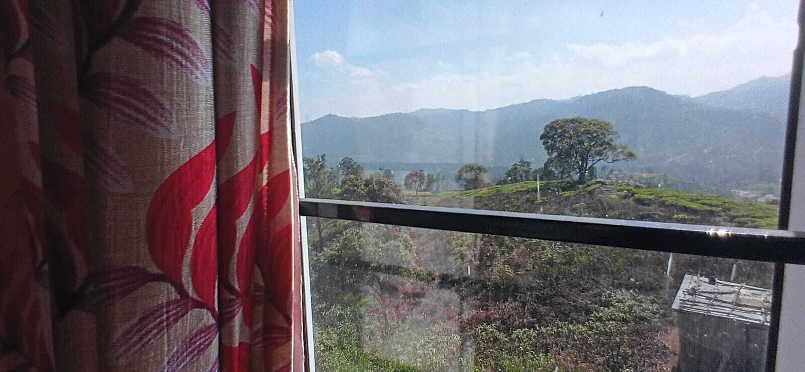 A window view of a mountainous landscape with greenery and trees.