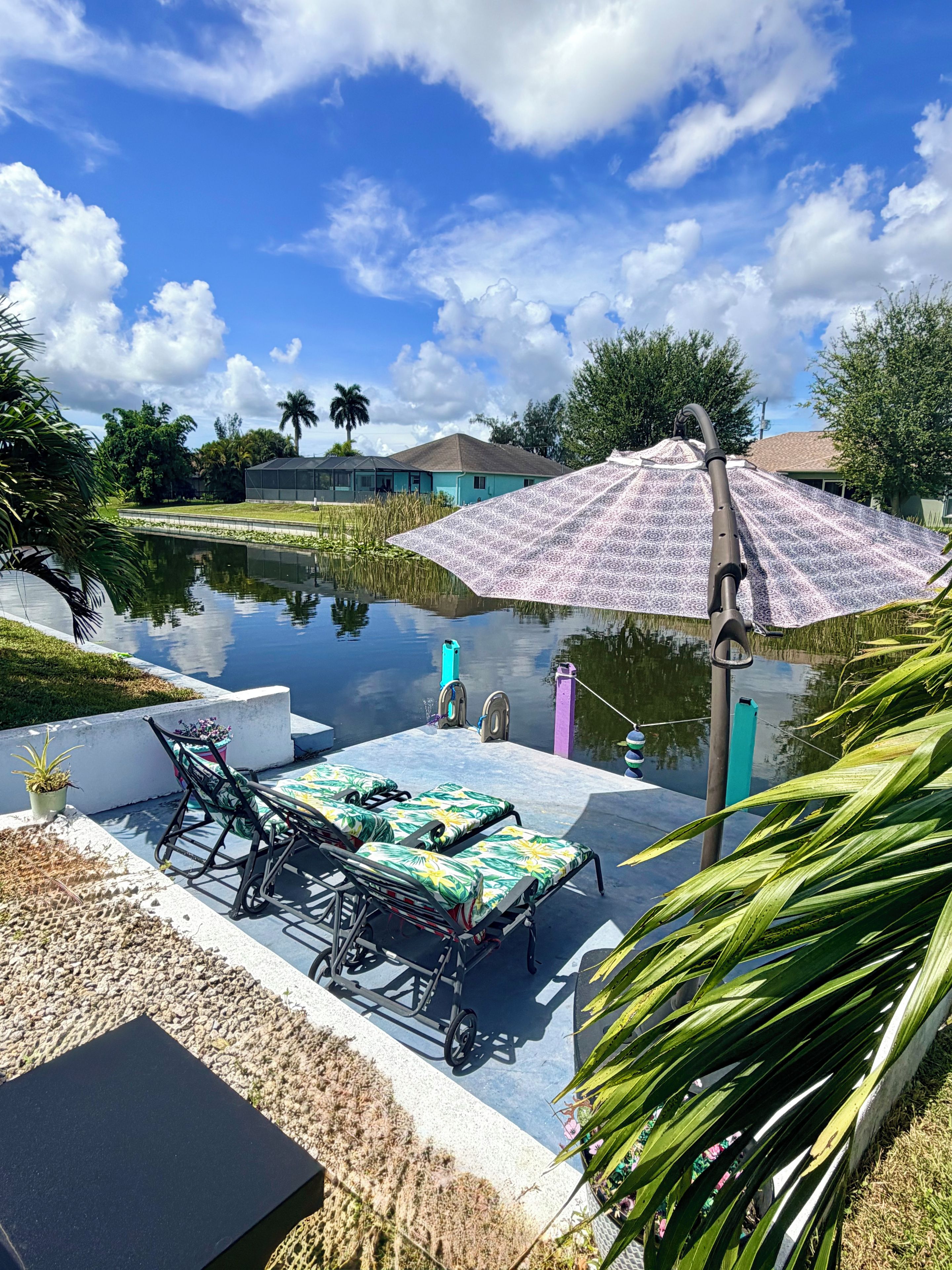 A tranquil outdoor seating area with a table and chairs, a covered umbrella, and a calm water body reflecting the sky.