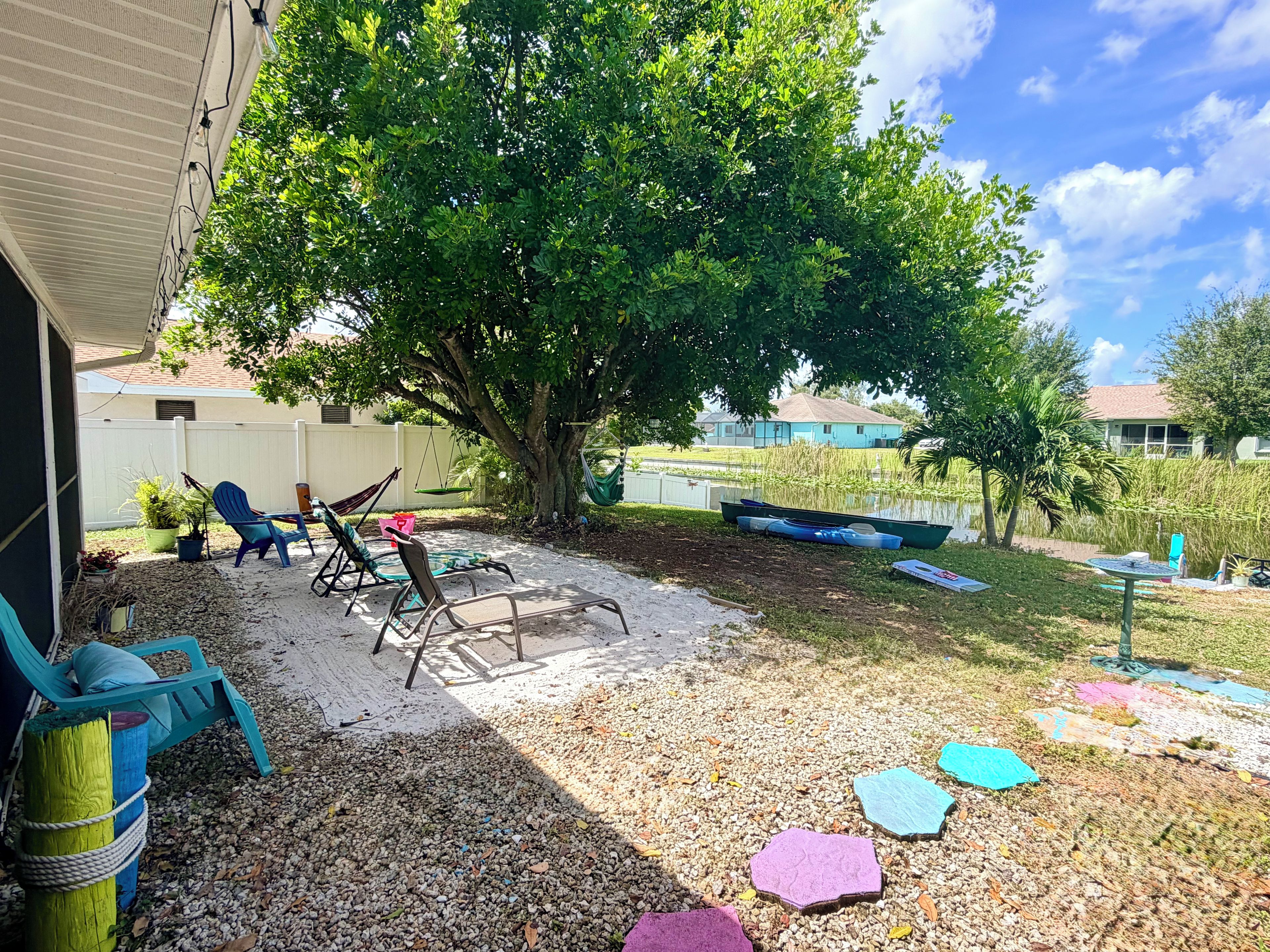 A backyard with a hammock, lounge chairs, a small pond, and a tree.