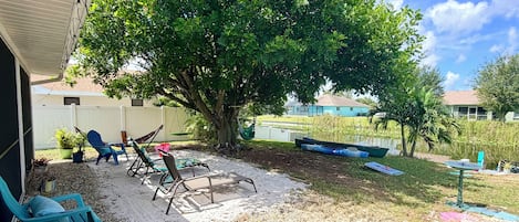 A backyard with a hammock, lounge chairs, a small pond, and a tree.