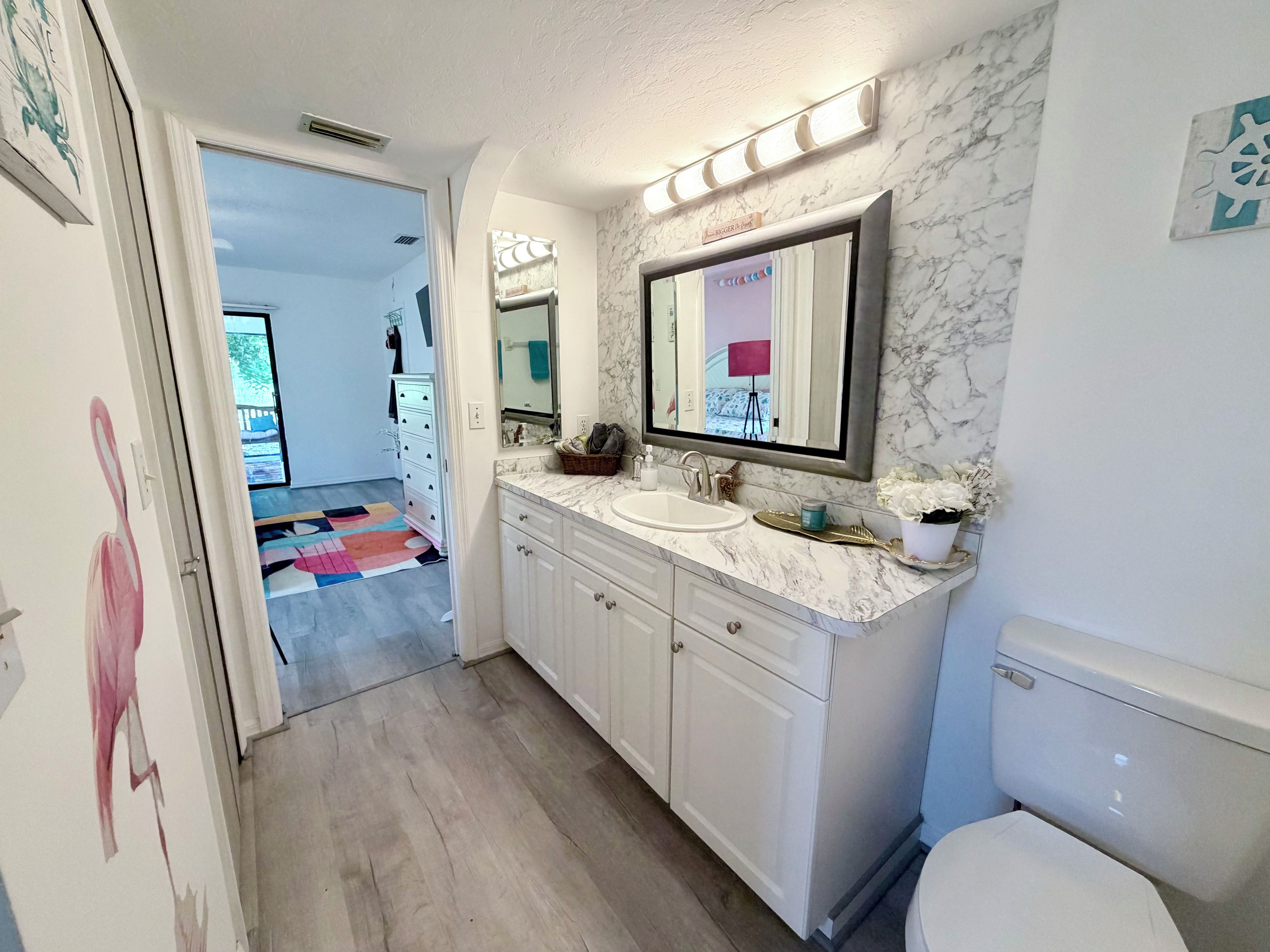 A bathroom with a marble countertop, a sink, a toilet, and a mirror with lights above.