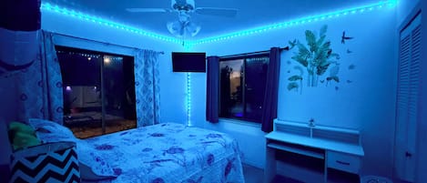 Un dormitorio con cama, ventilador de techo, ventana y pared con un adhesivo de planta.