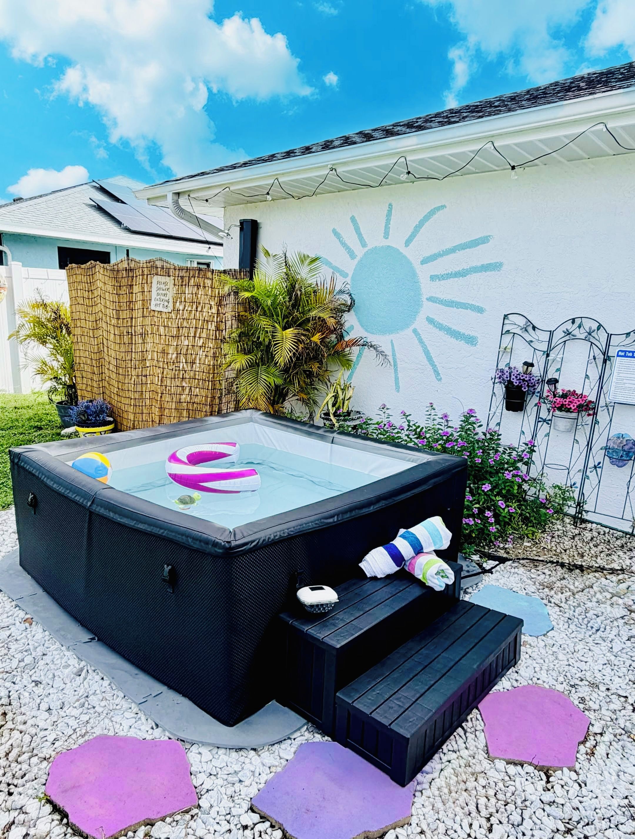 Ein Whirlpool mit Stufen, umgeben von einem Garten mit verschiedenen Pflanzen und einer Wand mit Sonnendekor.