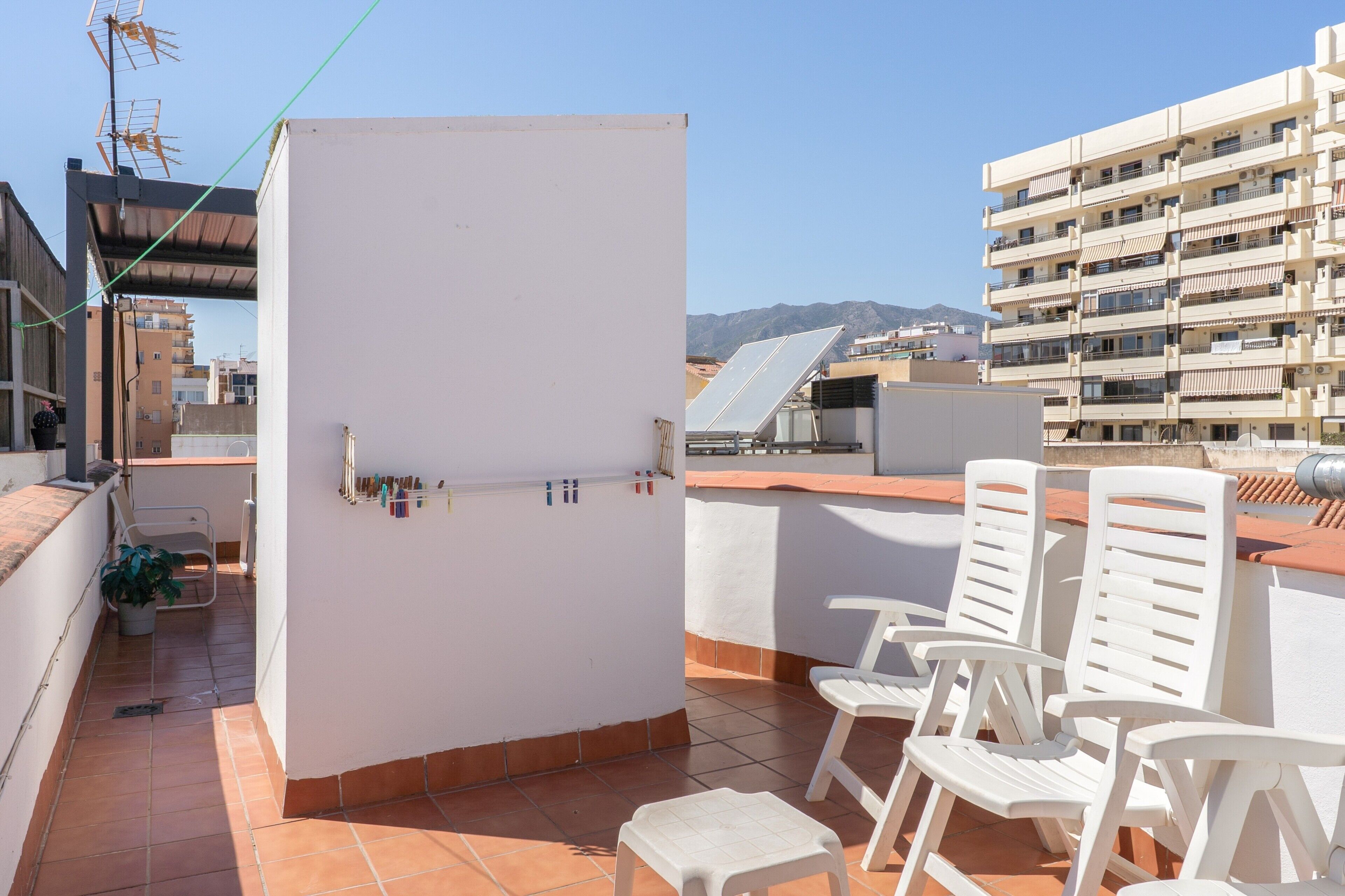A rooftop terrace with white chairs, a white cabinet, and a solar panel.