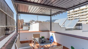 Une terrasse sur le toit, avec une table et des chaises, un pot de fleurs et des panneaux solaires installés sur le bâtiment.