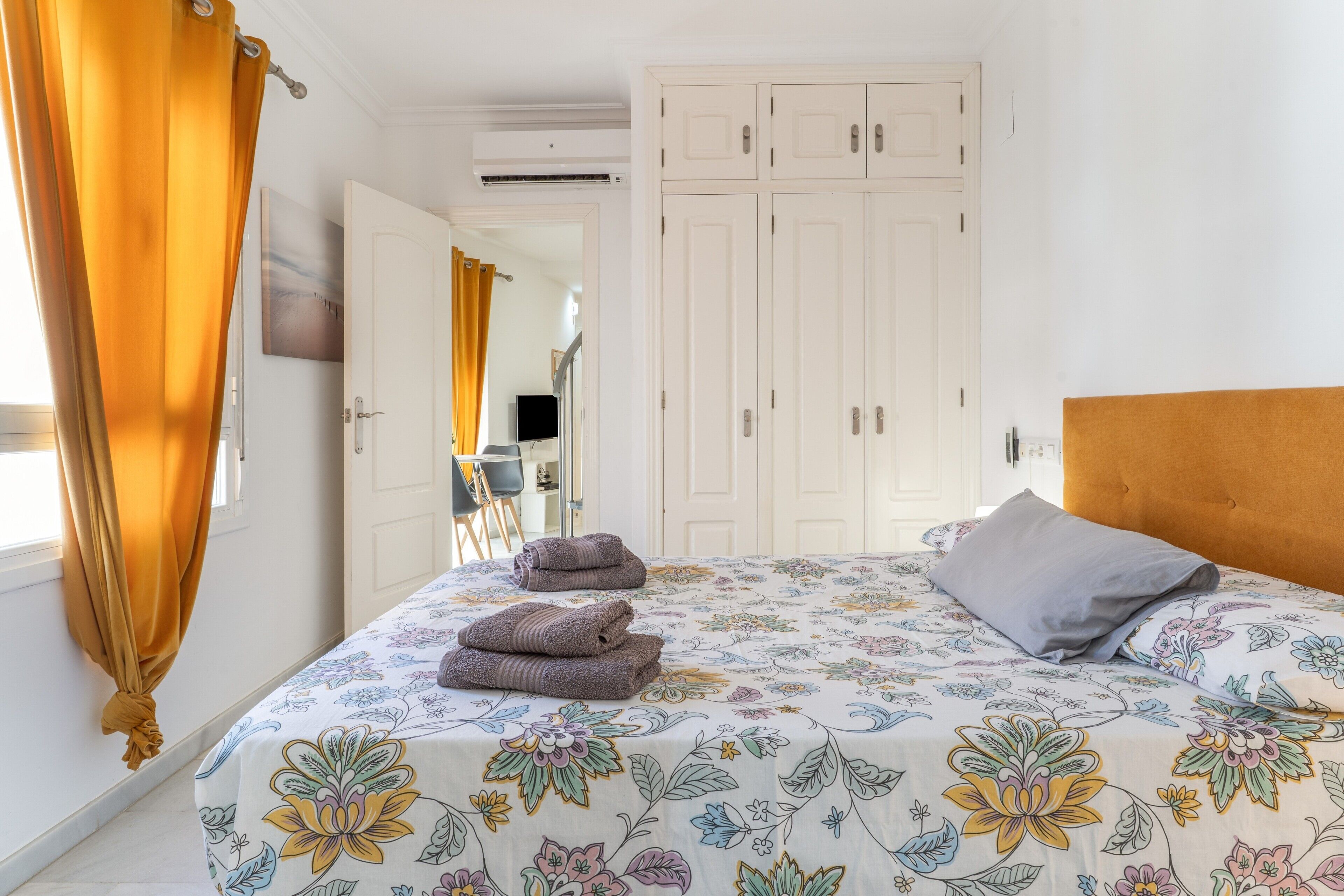 Ein Schlafzimmer mit Bett, Kopfstütze, Kleiderschrank und einem durchgehenden Türrahmen erkennbaren Badezimmer.