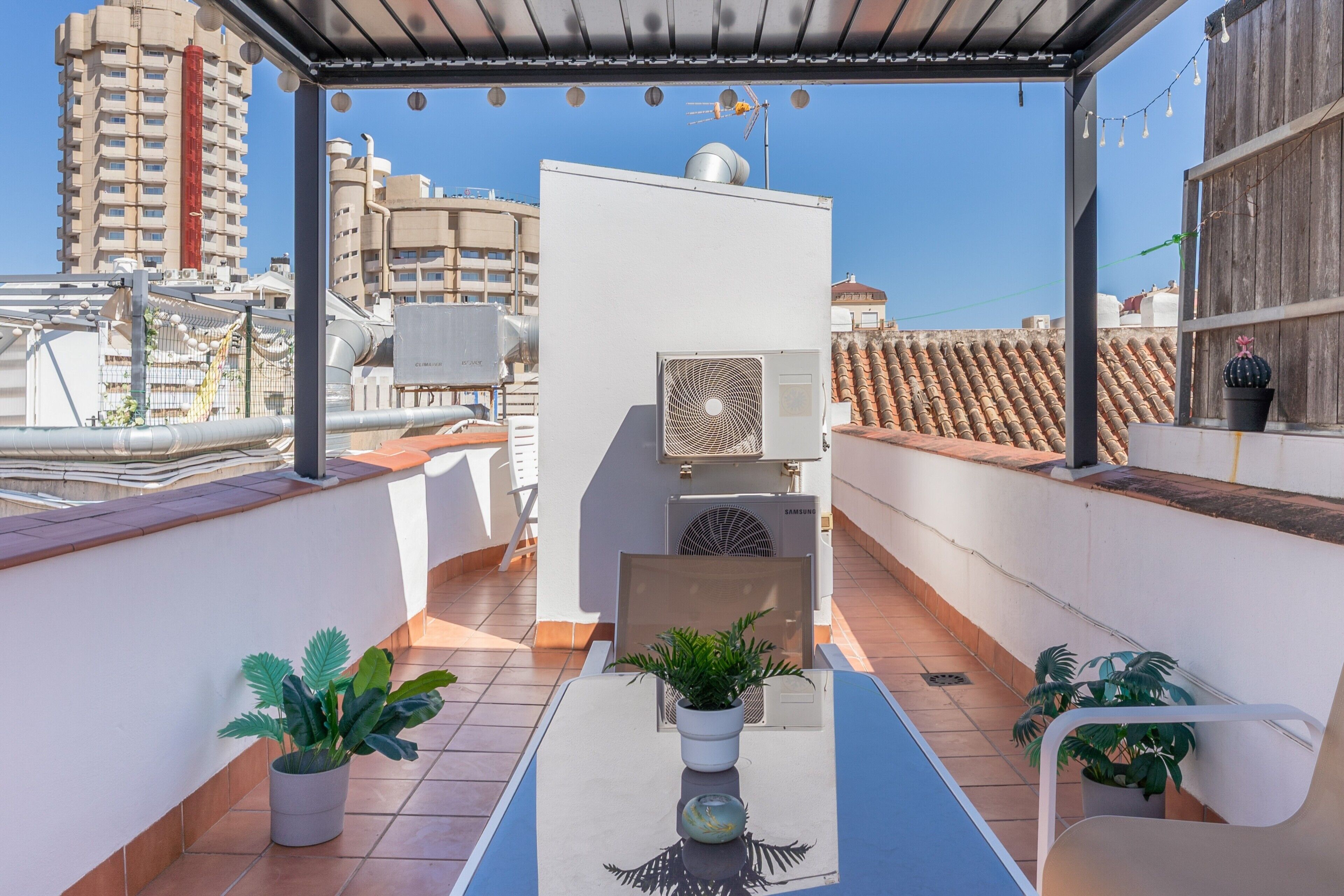 Eine Dachterrasse mit Topfpflanzen, einer Samsung-Klimaanlage und Blick auf die Stadtlandschaft.