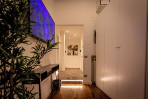 Ein Flur mit Holzboden, einer weißen Wand mit blauer Beleuchtung, einer Pflanze und einer Tür.