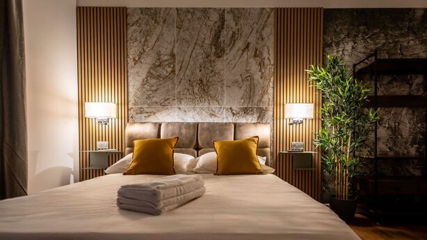 Ein modernes Hotelzimmer mit einem großen Bett, zwei Nachttischlampen, einem Marmorkopfstück und einer Bambuspflanze.