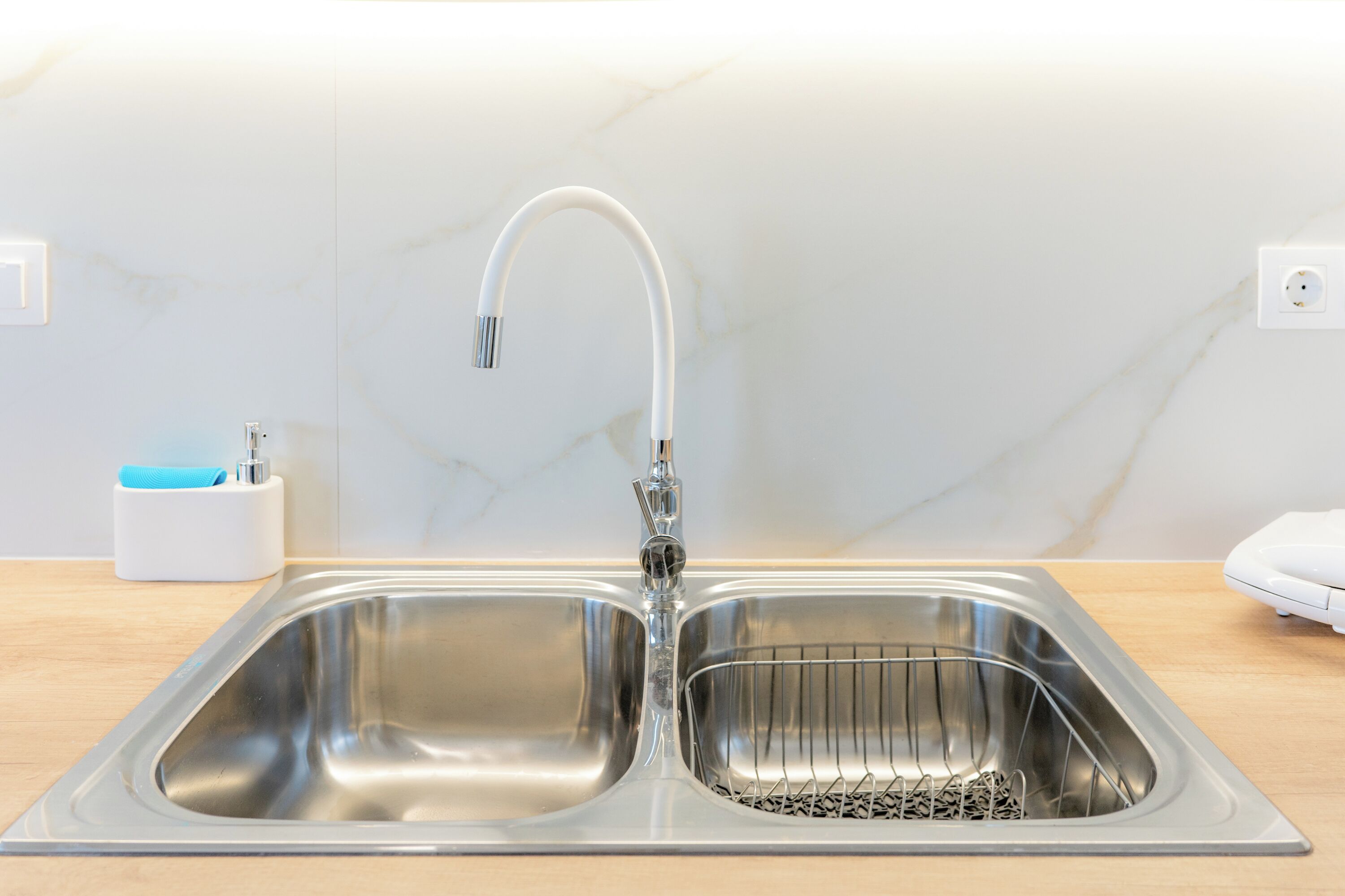 Un évier de cuisine en acier inoxydable, doté d’un robinet moderne, d’un distributeur de savon et d’une prise électrique murale.