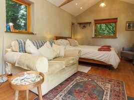 Un dormitorio acogedor con cama, sofá, una mesita y ventana con vistas a árboles.
