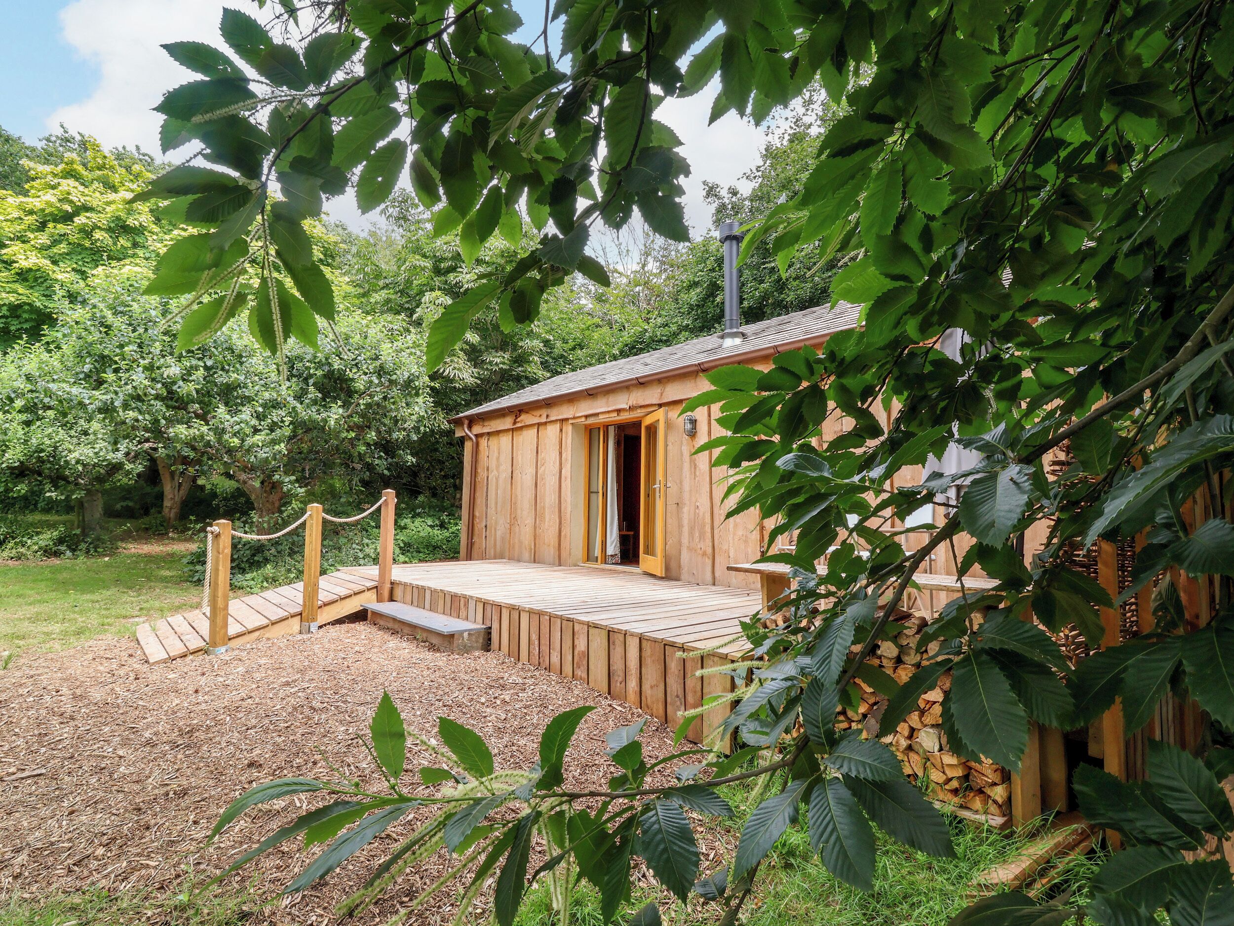 Une cabane en bois dotée d’une terrasse, entourée d ’arbres et d’un jardin.