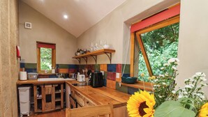 A kitchen with wooden cabinets, a sink, and a window with a view of greenery. - Brambly Cabin (Crediton)