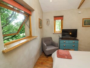Ein Schlafzimmer mit einem Bett, einem Fernseher auf einer Kommode, einem Sessel und einem Fenster mit Blick auf Bäume.