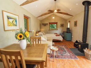 Una habitación acogedora con cama, una mesa y sillas, un jarrón de girasoles, una alfombra y un estufa de leña.