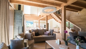 A spacious living area with a wooden ceiling, a large sofa, a coffee table, and a staircase leading to an upper level. - R Sidence Les Portes de Meg ve C614 (Praz-sur-Arly)