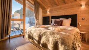 A wooden cabin bedroom with a large bed, a window with curtains, and a view of a snowy landscape. - R Sidence Les Portes de Meg ve C614 (Praz-sur-Arly)