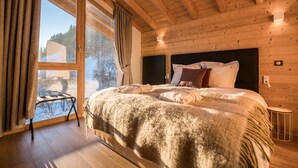 Un dormitorio de cabaña de madera con una cama grande, una ventana con cortinas y vistas a un paisaje nevado.