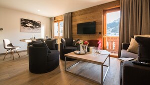 Una sala de estar moderna con piso de madera, un televisor de pantalla plana en la pared, un comedor con mesa y sillas, y un balcón con vistas a las montañas.