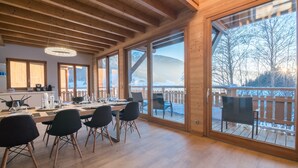 Un comedor amplio con una mesa larga y sillas, ventanas grandes con vistas a un paisaje nevado, y vigas de madera en el techo.