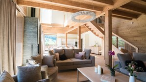 Een ruime woonkamer met een houten plafond, een grote bank, een salontafel en een trap naar een hoger gelegen verdieping.