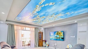 Ampla sala de estar com um mural no teto, TV de tela plana e um espaço para sentar.